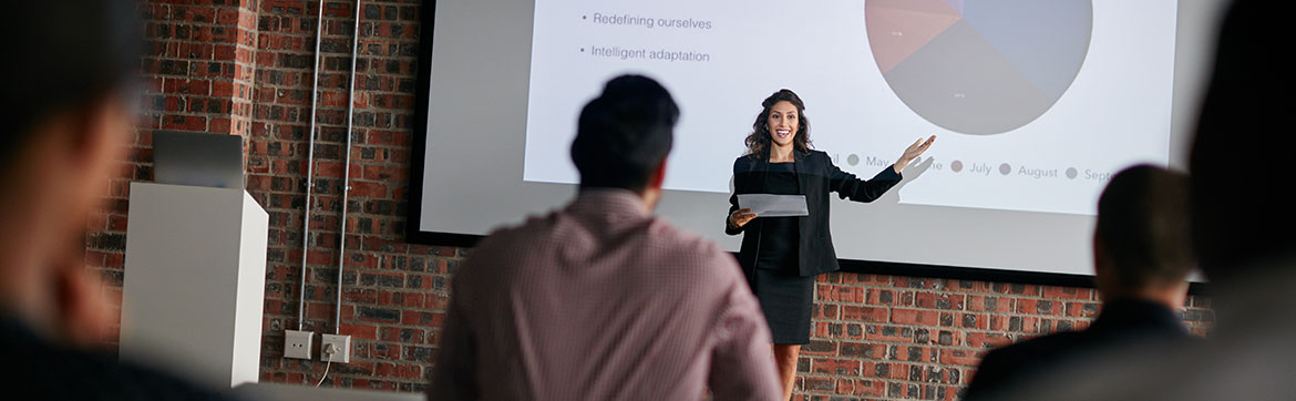 A lady presenting on stage in front of a group