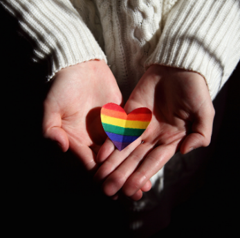 A picture of a person cradling a multi-coloured heart shaped piece of paper. (Pexels | Sharon McCutcheon)