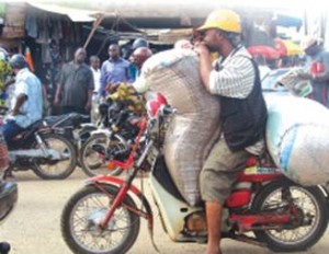 Image of a man holding a bag of grains on a red motorcycle. 