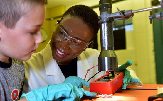 Member of staff helps a child with a scientific experiment 