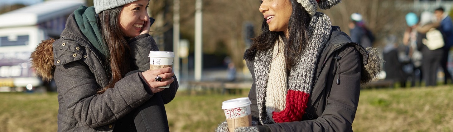 Two students drinking coffee outside.