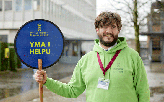 Llysgennad myfyrwyr yn dal arwydd 'Yma i Helpu'