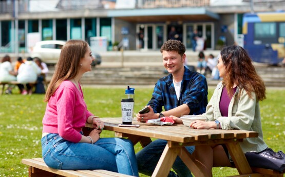 three students happily sitting on a table outside Fulton House