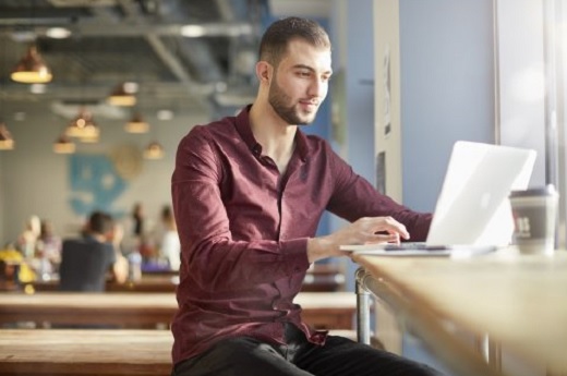 Man in red shirt sitting at a table with a laptop