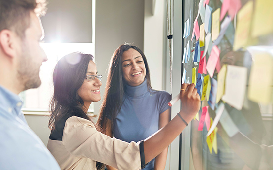 Writing on Post-it notes on white board - team working 