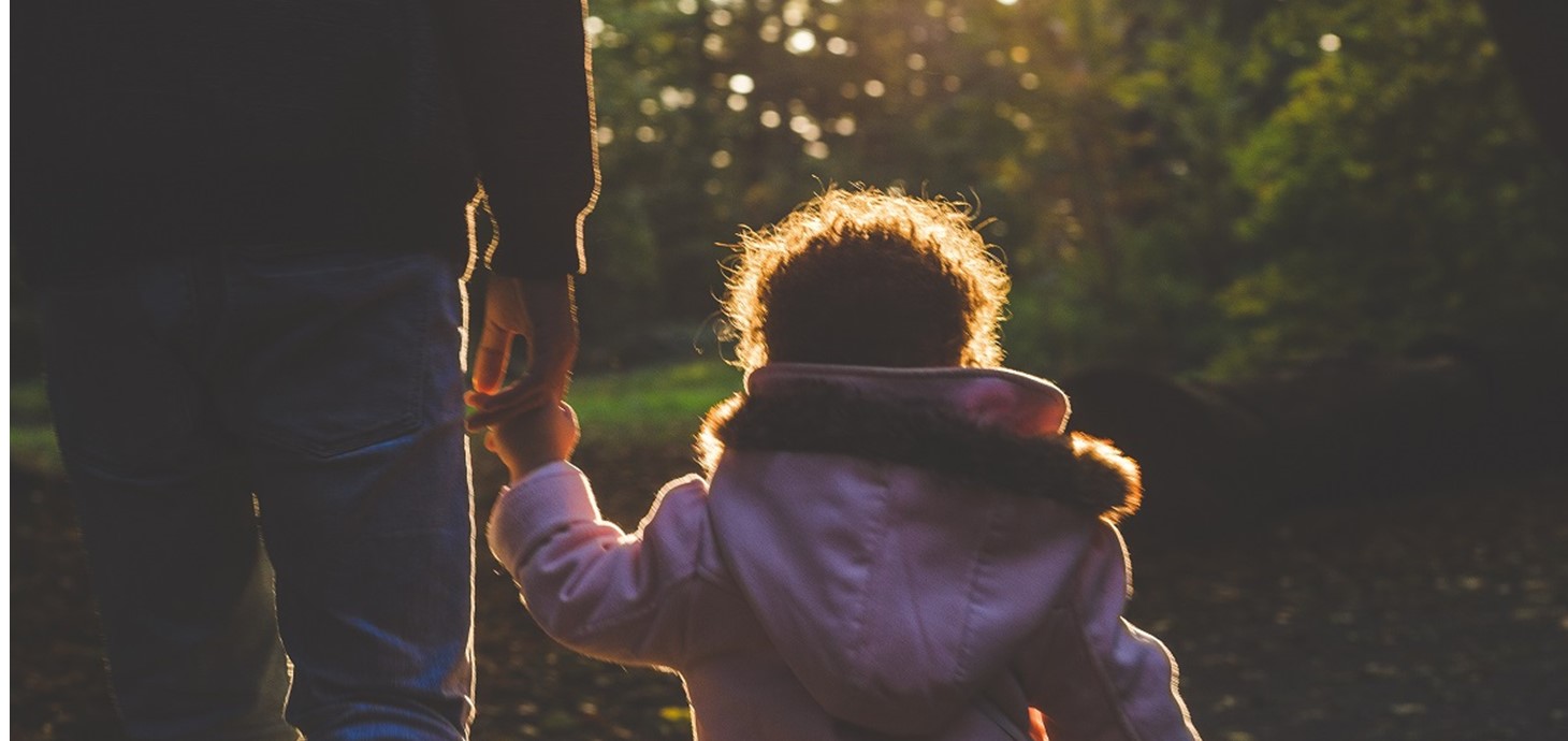 Child and carer hand in hand walking away from the camera