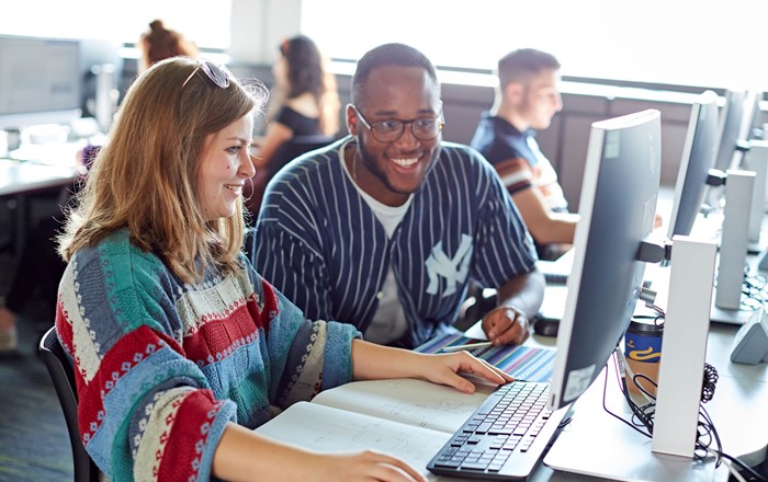 Two students sitting working in a computer lab.