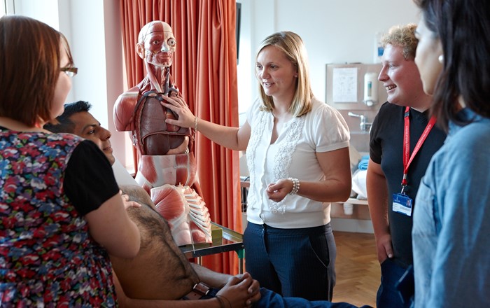 Group of students in medical practice class looking at a skeleton while listening to a lecturer