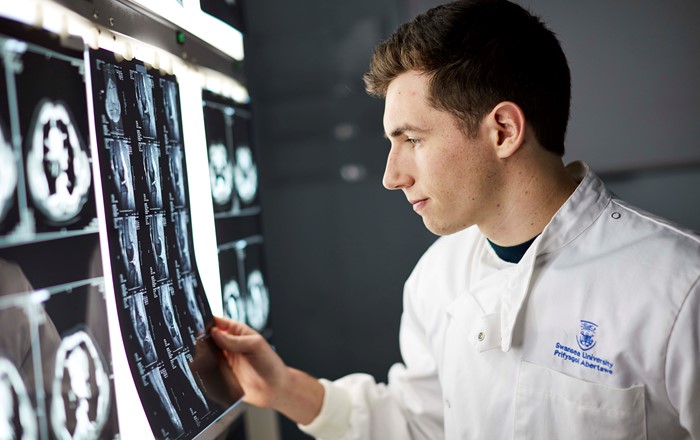 Male medical student wearing white coat looking at scan images on a light box