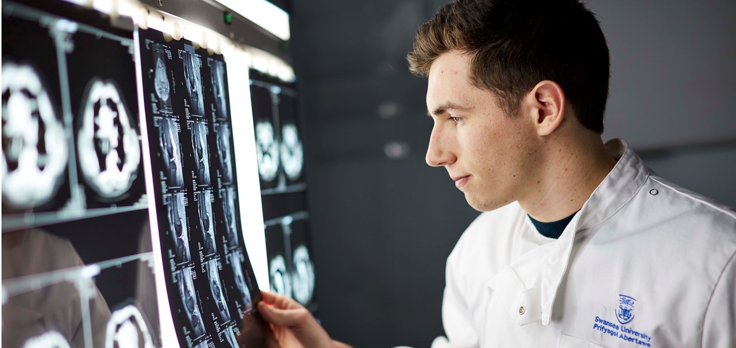 Male medical student wearing white coat looking at scan images on a light box