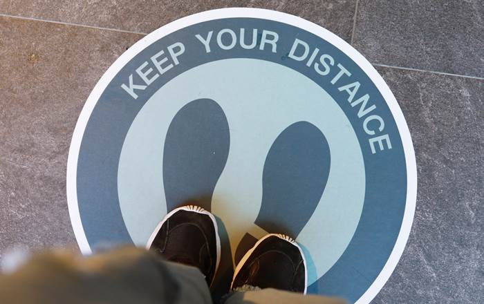 A person standing on a floor sign that reads 'Keep your distance' 