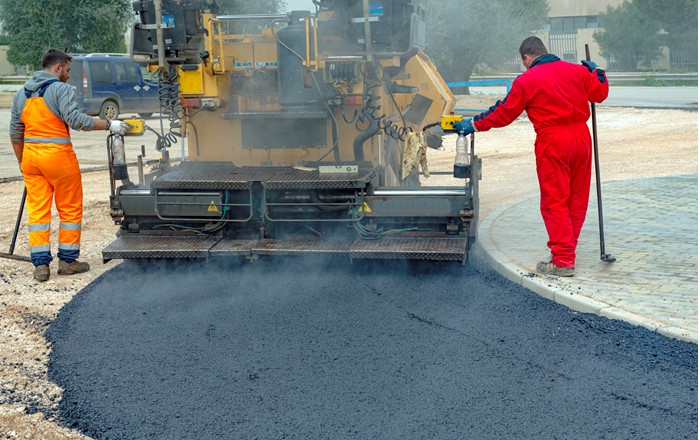 Two men spreading tarmac onto road.