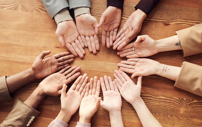 Picture of six pairs of hands held out palms upwards in a circle on table