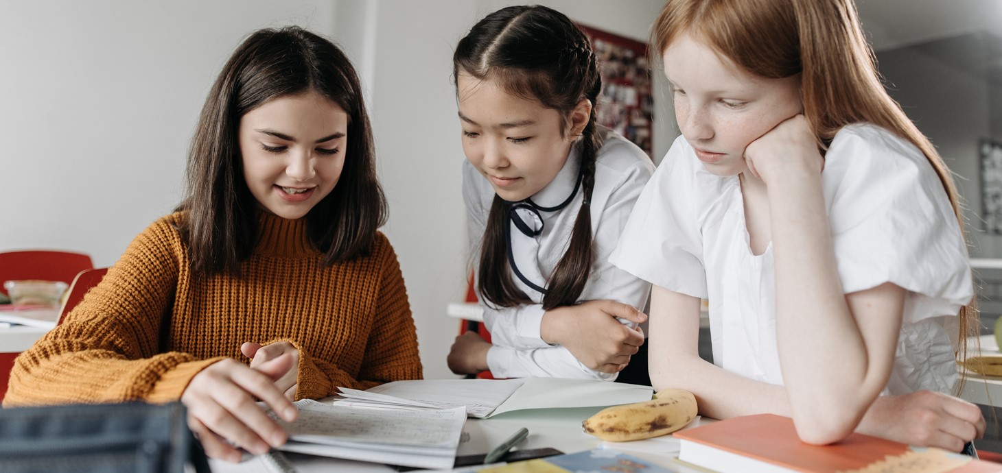 Three young schoolgirls in a classroom studying at a desk 