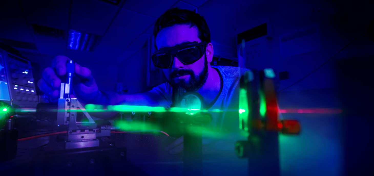 Scientist wearing goggles conducting an experiment using a laser in a darkened room