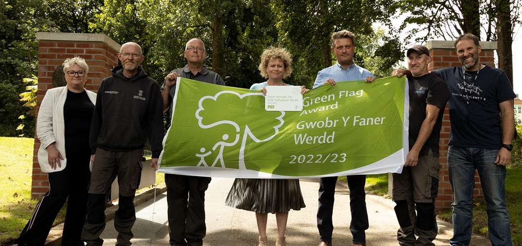 Group of people outside standing in a line holding a green flag