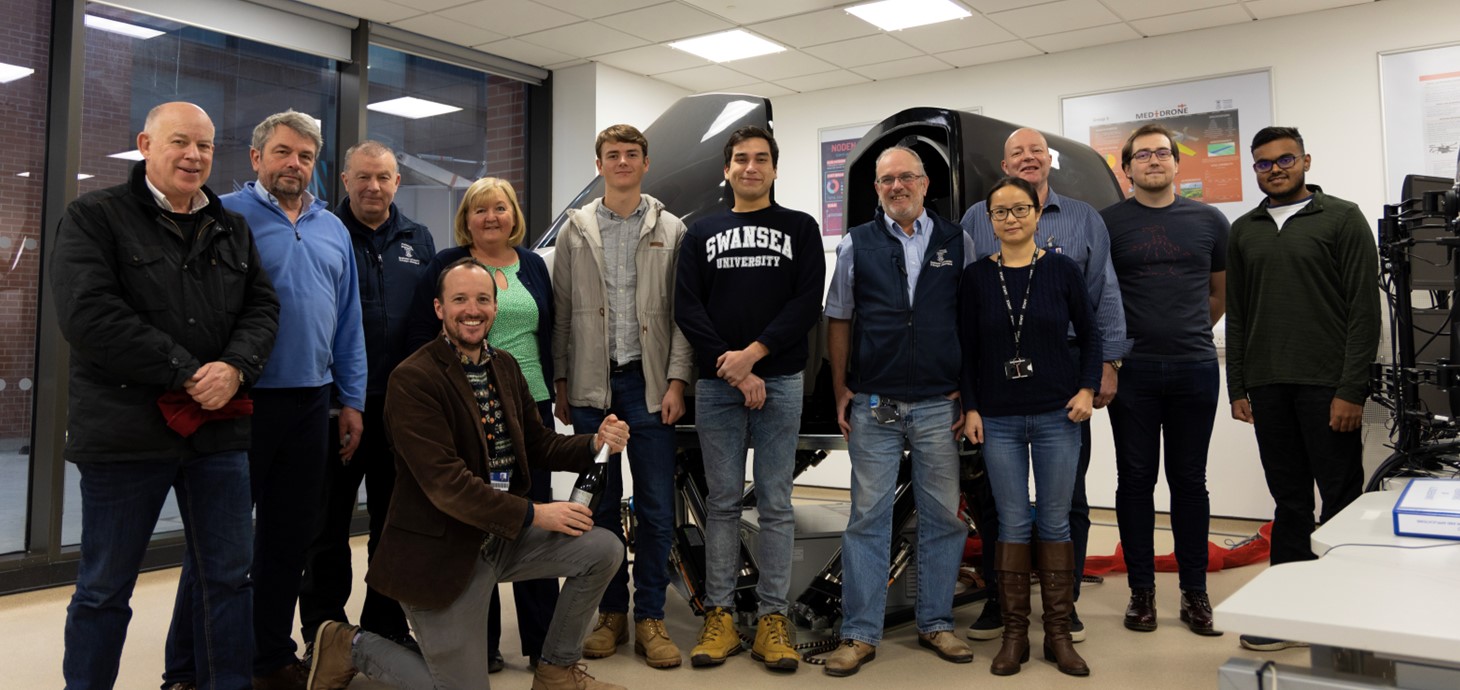 Group of people standing in a room in front of flight simulator.