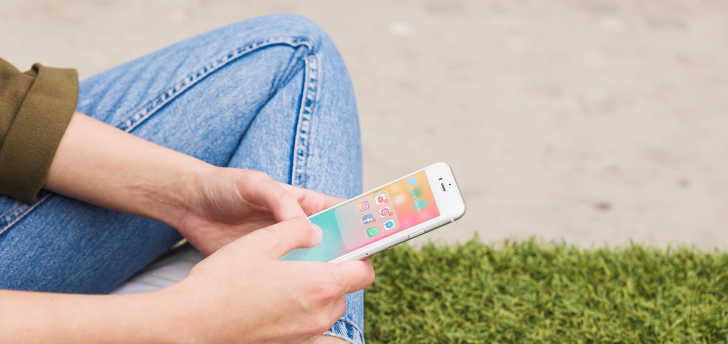 A person sits on the floor as they search for social media apps on their phone.