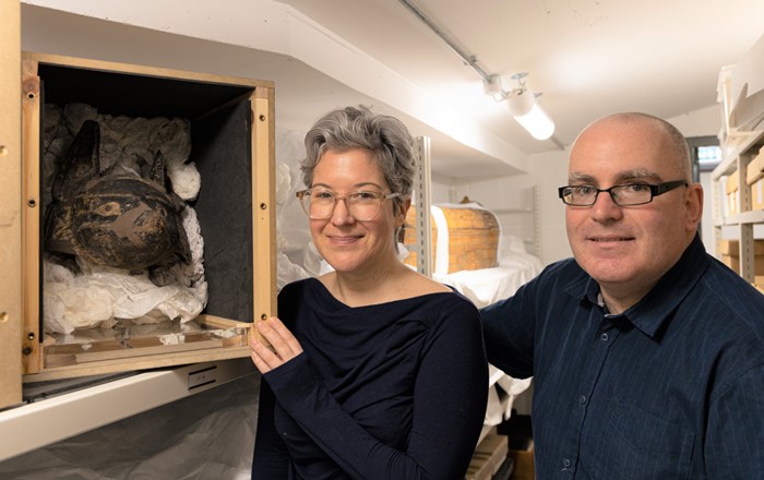 Man and woman standing in a storeroom alongside an open box containing an Egyptian artefact