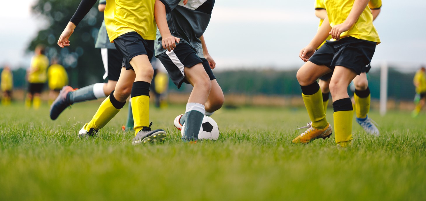 Youngsters pictured from chest down playing football on an outdoor pitch