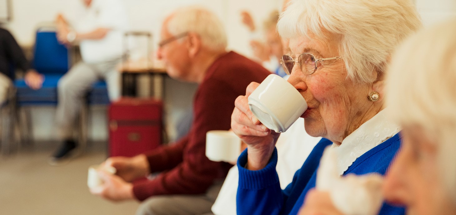 A close up shot of an elderly woman drinking tea with friends.