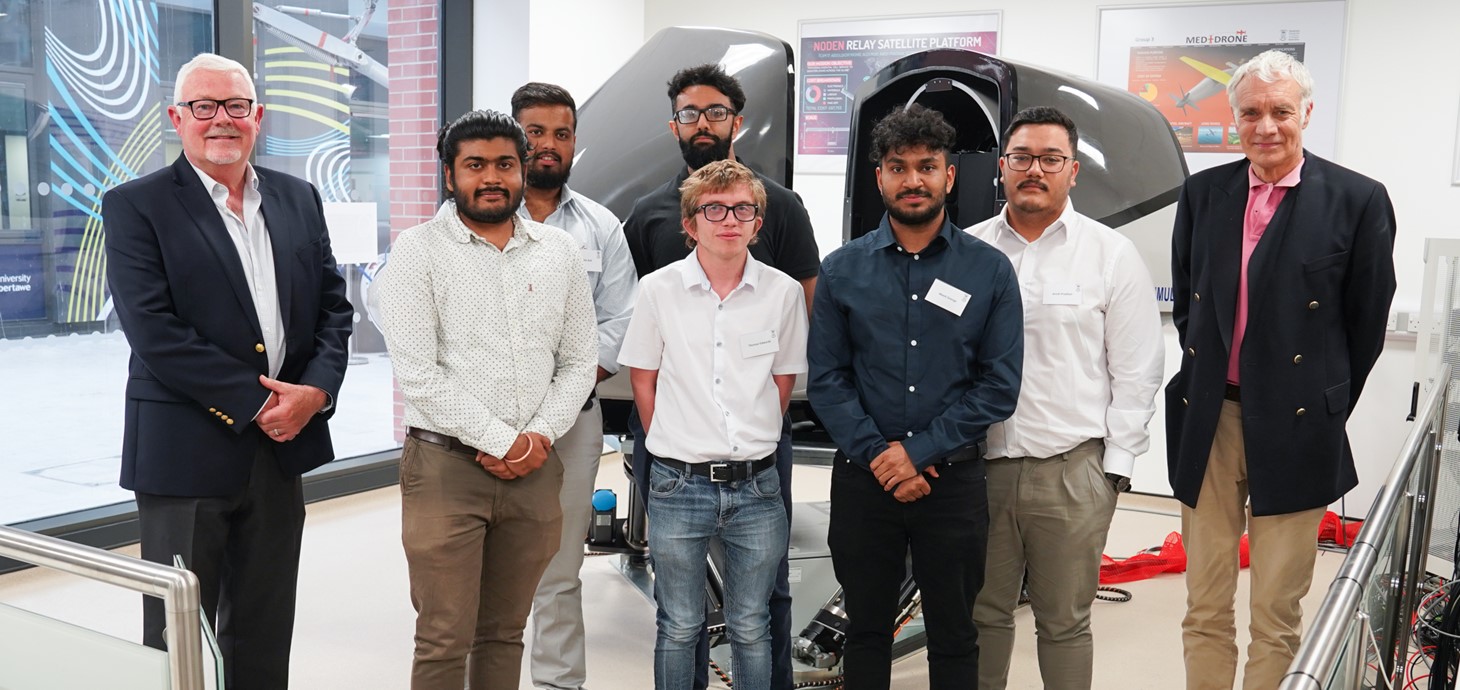 Group of students standing in front a flight simulator with two older men