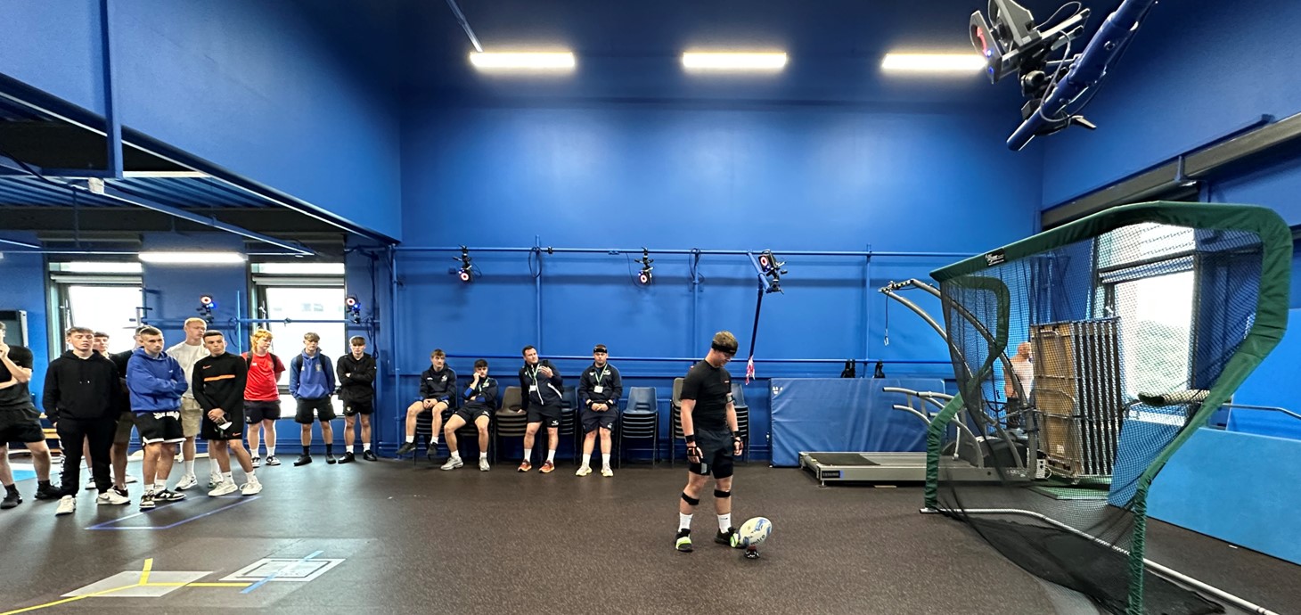 A group of students watching as one gets ready to kick a rugby ball.