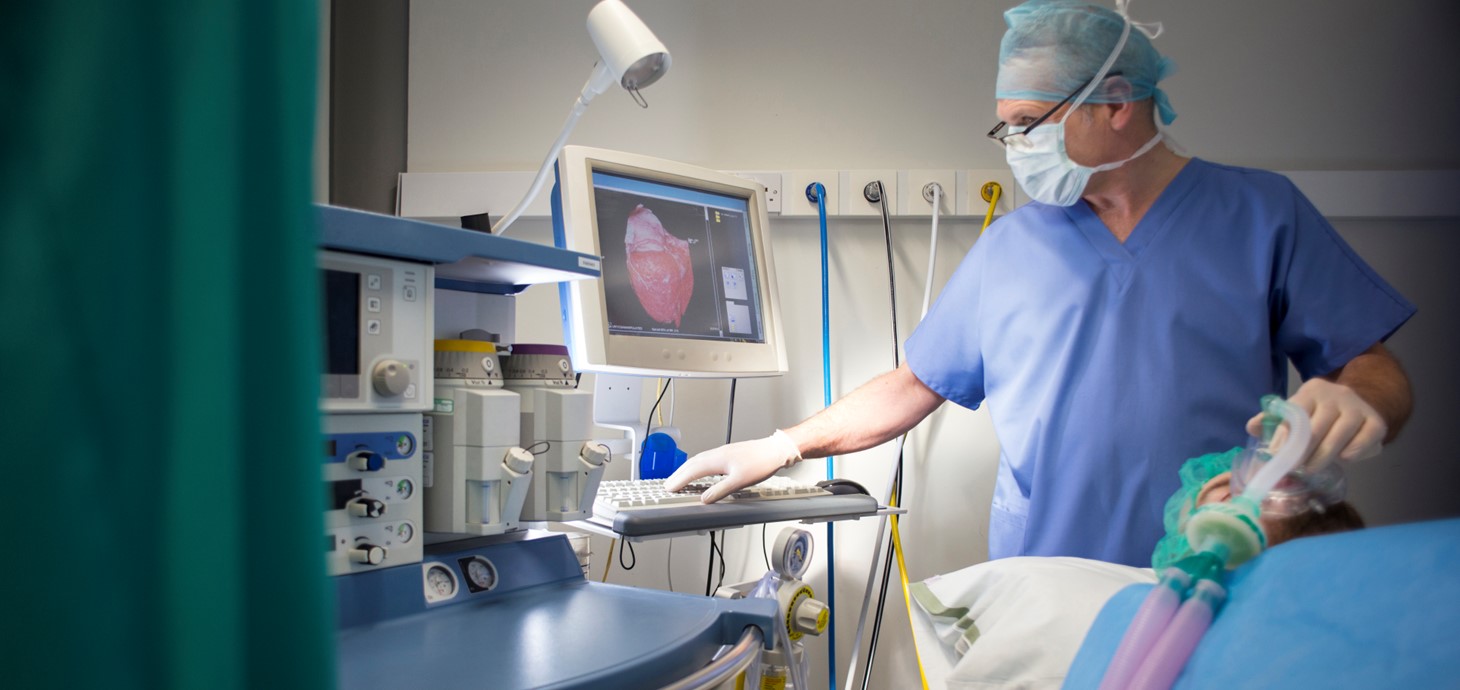 Anesthetist in a hospital room, standing by side of a patient lying down. 