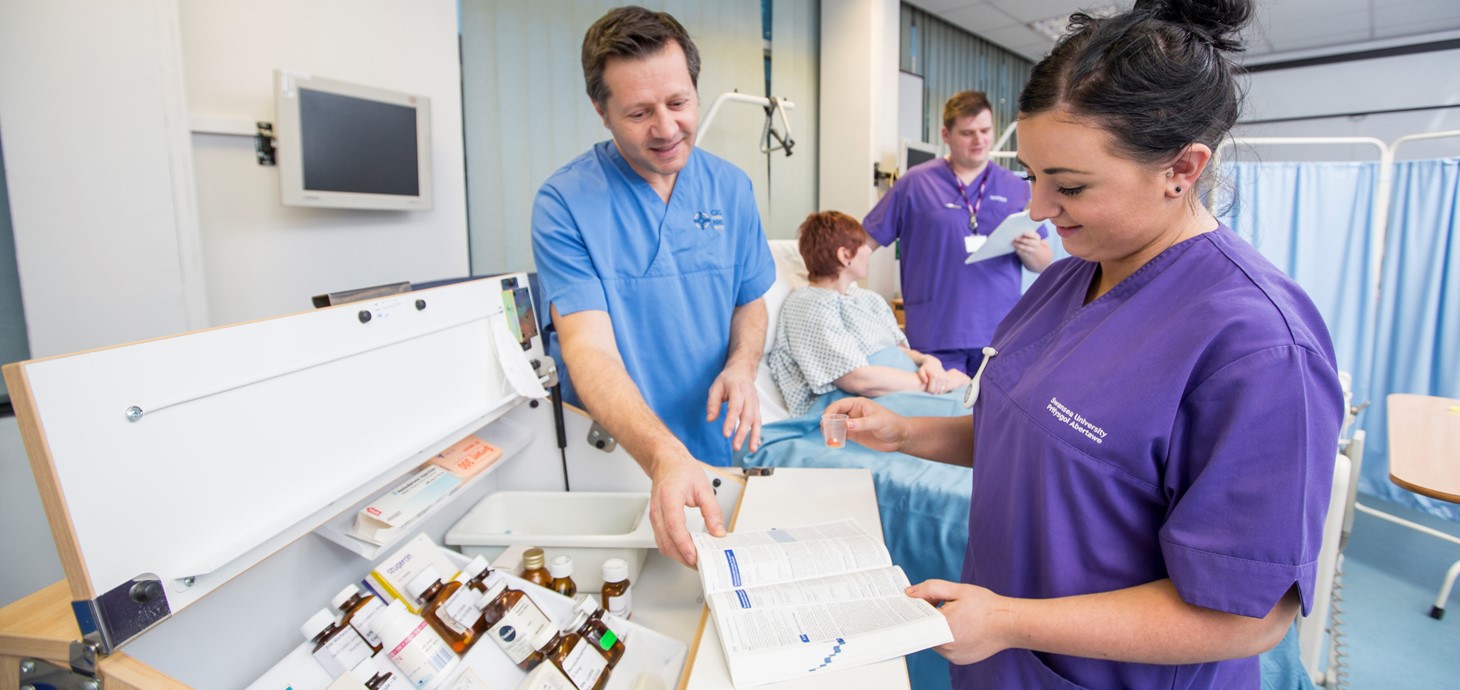 Nurses in uniform on a ward looking at charts by a drugs cabinet