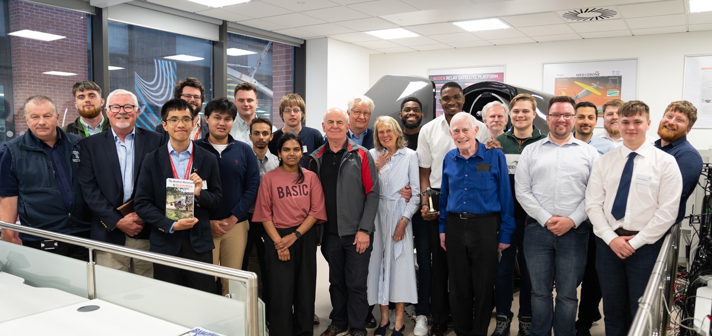 Group of 21 people standing indoors in front of a flight simulator 