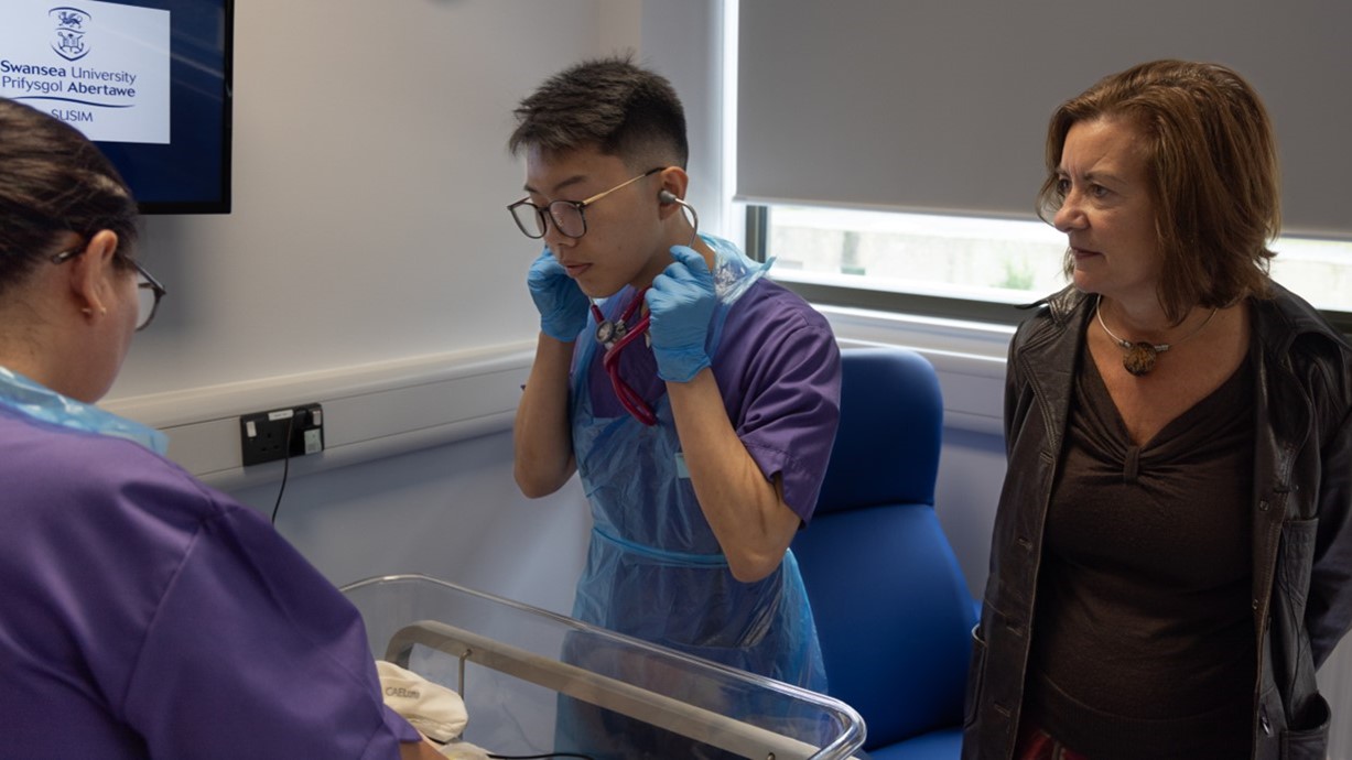 First Minister of Wales, Eluned Morgan MS, is watching two nursing students practicing baby care in the Simulation and Immersive Learning Centre at Swansea University.