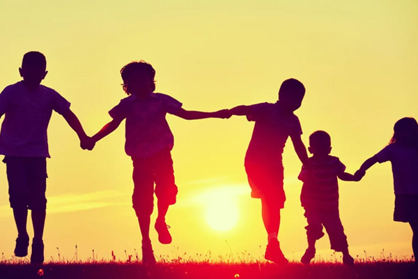 Children holding hands running with the sun in the background