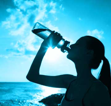 A young woman drinking a bottle of water with the sea in the background