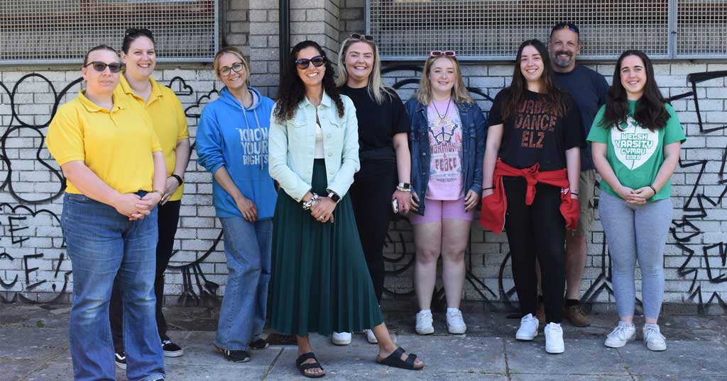 Lella and students smiling and standing in front of artwork 