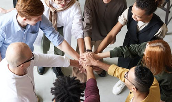 A diverse group of people stood in a circle with their hands on top of each otehr