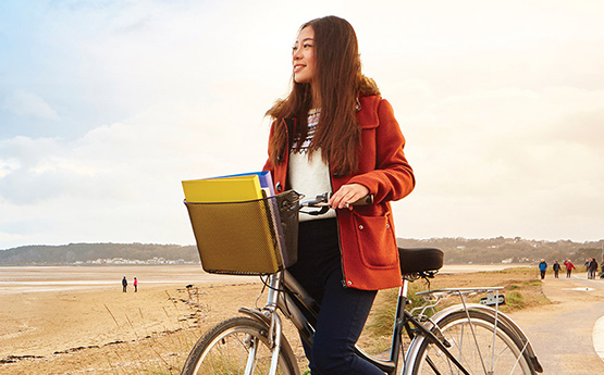 Student smiling outside in the sun on a bike.